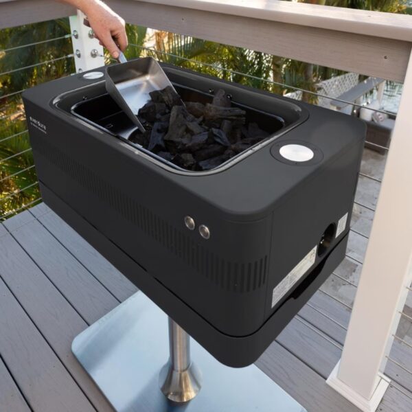 Modern charcoal grill on a patio, featuring a sleek design and a hand holding a metal scoop over a container filled with charcoal.