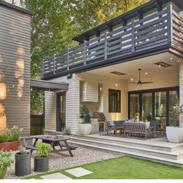 Modern backyard patio featuring a stylish outdoor seating area, grill, and greenery, complemented by a second-floor balcony with railing.