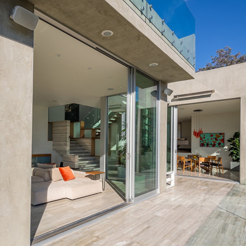 Modern living room with large glass doors, showcasing an open floor plan, stylish furniture, and a view of the dining area and staircase.