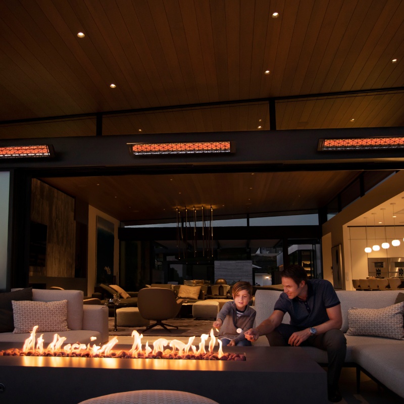 Father and son enjoying quality time by a modern fire pit in a stylish indoor-outdoor living space with warm lighting.