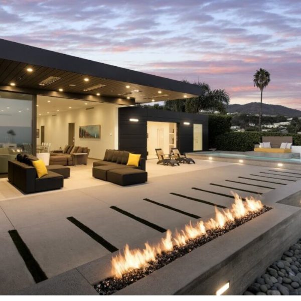 Modern outdoor living space featuring a sleek patio with a fire feature, comfortable seating, and a swimming pool at sunset.
