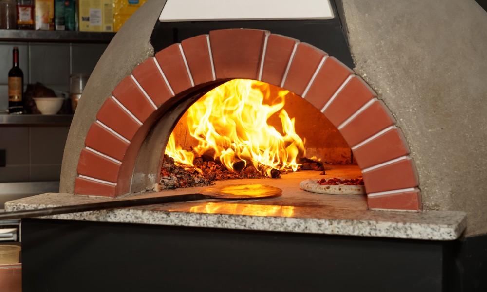 Wood-fired pizza oven with flames and pizza dough inside, showcasing traditional cooking methods.