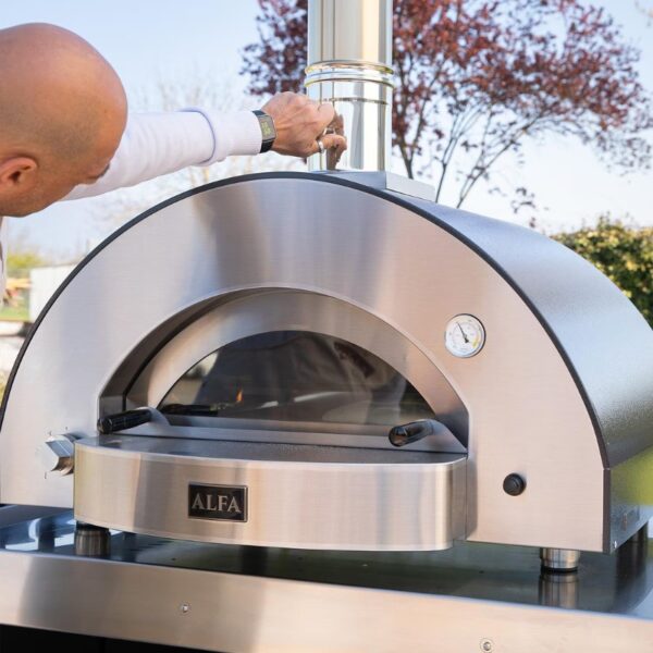 Person adjusting the chimney on an Alfa outdoor pizza oven, showcasing its stainless steel design and built-in temperature gauge.