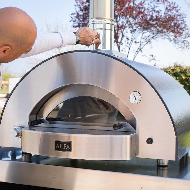 Close-up of a person adjusting the chimney of an Alfa outdoor pizza oven, showcasing its stainless steel design and built-in temperature gauge.
