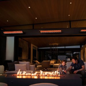 Family enjoying time together by a modern fire pit in a stylish outdoor living space, with heating lamps overhead providing warmth.