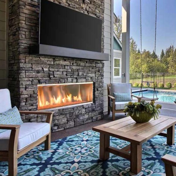 Cozy outdoor living space featuring a stone fireplace, modern TV, comfortable seating, and a swimming pool in the background.