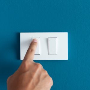Hand pressing a light switch on a blue wall, illustrating home lighting control.