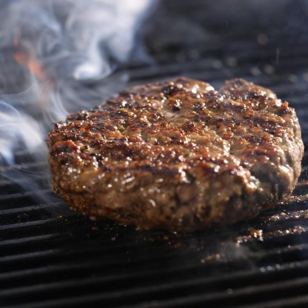 Grilled beef burger patty sizzling on the barbecue with smoke rising, showcasing a juicy and flavorful texture.