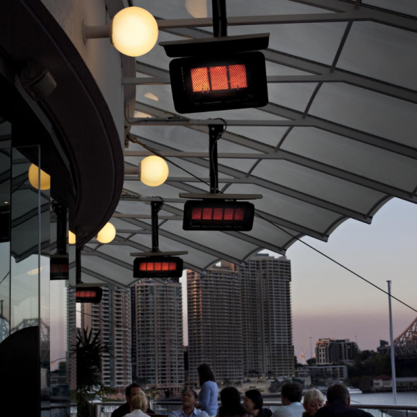 Outdoor dining area with hanging infrared heaters and ambient lighting, overlooking a city skyline at sunset.