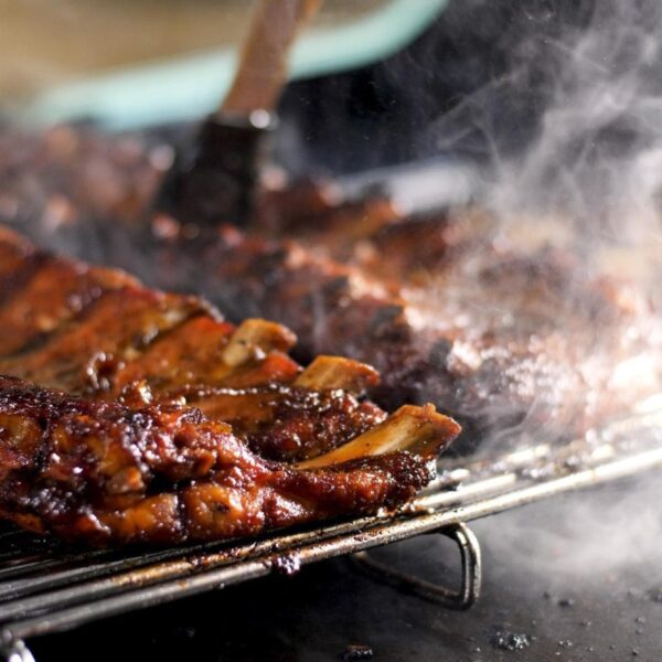 Close-up of smoky grilled ribs glistening with barbecue sauce on a rack, showcasing a deliciously charred texture.