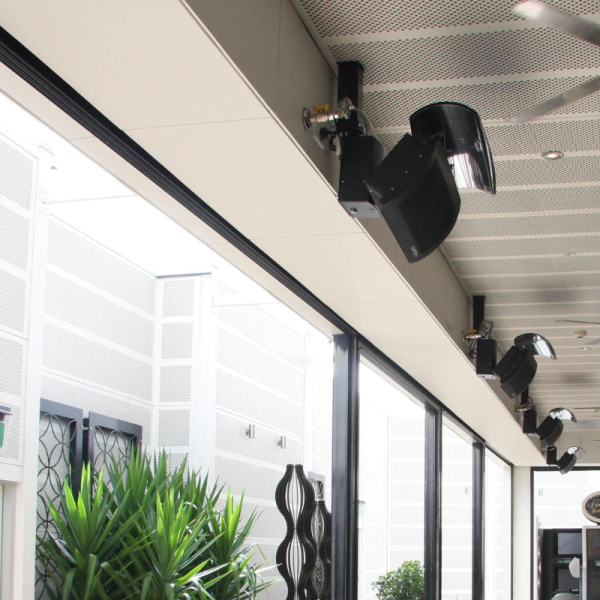 Interior view of a modern space featuring ceiling-mounted speakers and stylish decor, with large glass windows and indoor plants.