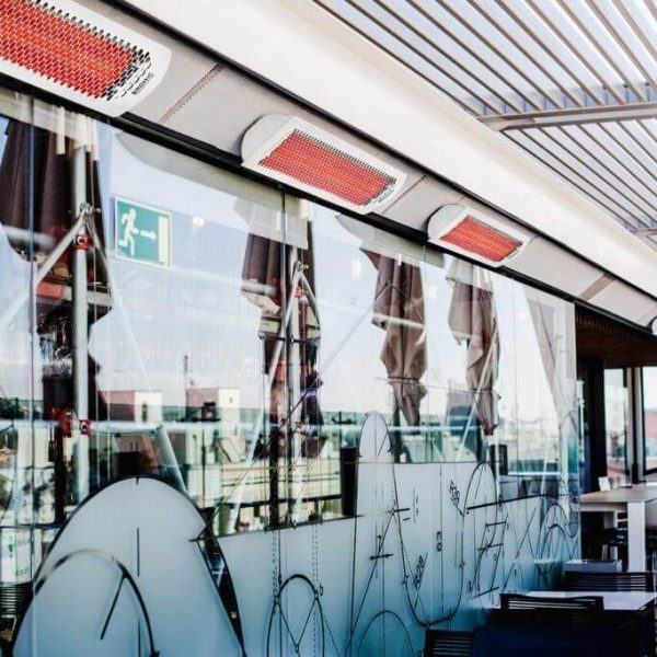 Outdoor patio with infrared heaters mounted above glass walls, featuring modern design and reflections of surrounding architecture.