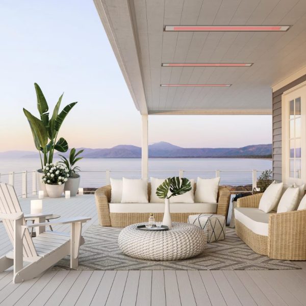 Stylish outdoor patio featuring a cozy seating arrangement with a woven sofa and chairs, decorative plants, and a scenic view of the water and mountains at sunset.