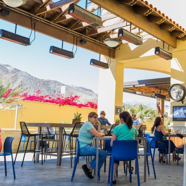 Outdoor dining area with patrons enjoying a meal under heating lamps, surrounded by mountain views and vibrant flowers.