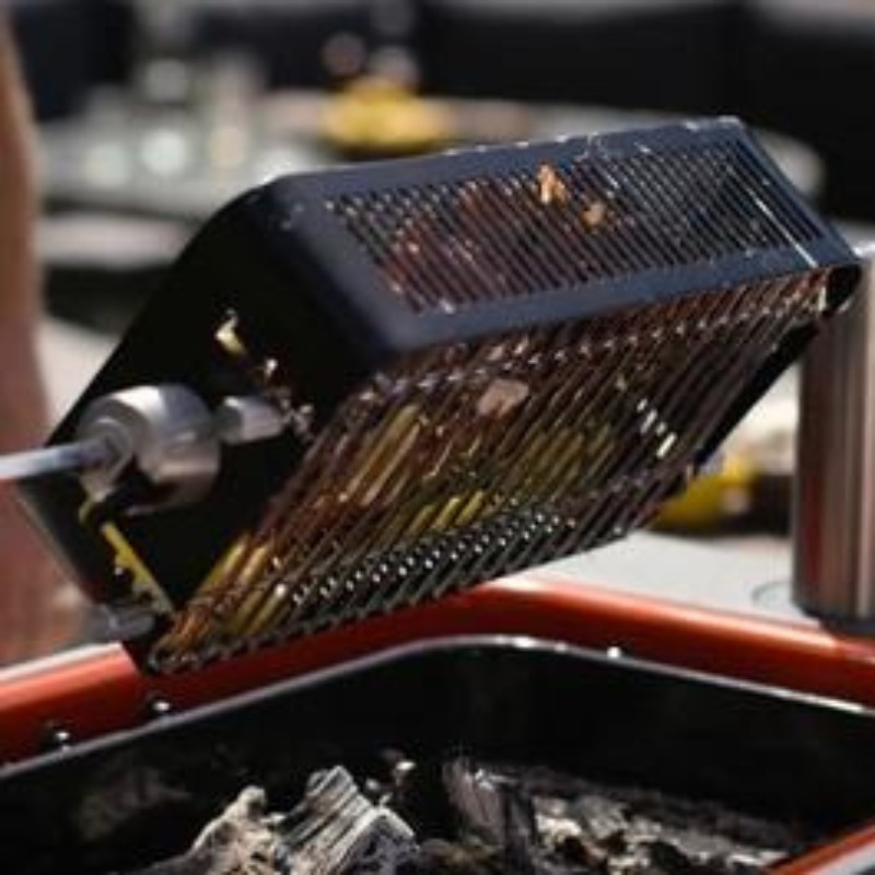 Grilling basket over a charcoal grill, showcasing a portable cooking tool for barbecuing vegetables and small foods outdoors.