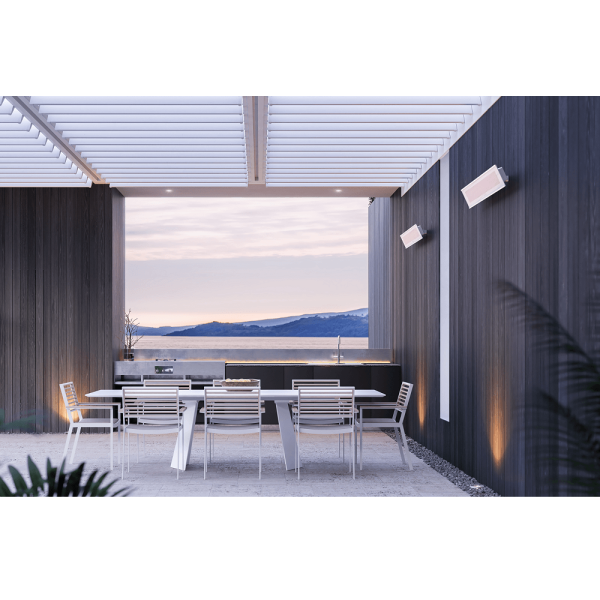 Modern outdoor dining area with a sleek table and chairs, featuring a kitchen setup and scenic mountain views at sunset.