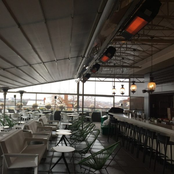 Modern rooftop restaurant interior featuring green chairs, white tables, and a sleek bar area with pendant lighting and heaters for comfort.