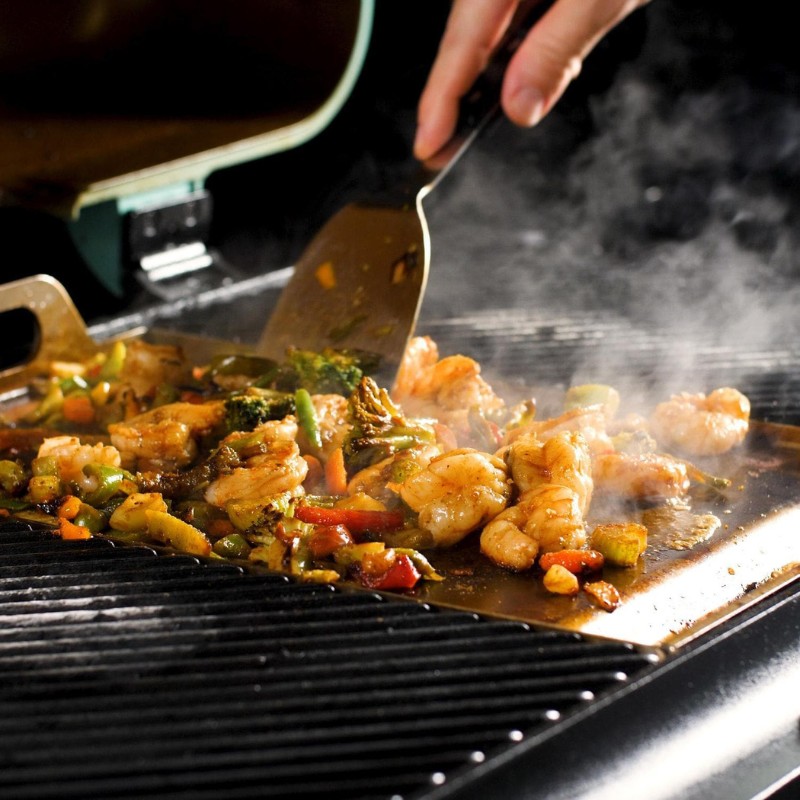 Grilling shrimp and vegetables on a hot grill, with steam rising and a spatula in hand.