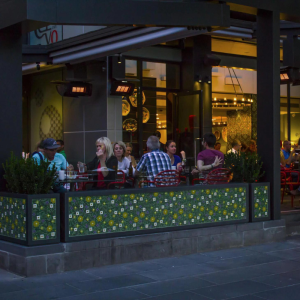 Outdoor dining scene at a restaurant with patrons enjoying meals and drinks, featuring decorative tiles and warm lighting.