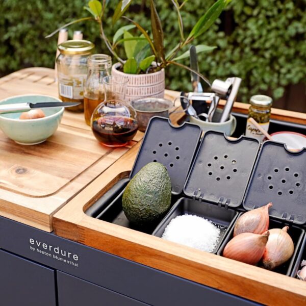 Modern outdoor kitchen setup featuring an Everdure by Heston Blumenthal countertop, with fresh ingredients like avocado, shallots, and salt, alongside cooking tools and condiments.