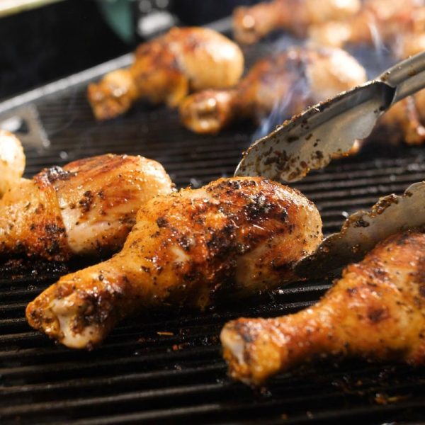 Grilled chicken drumsticks with smoky seasoning on a barbecue grill, showcasing a close-up of the cooking process.