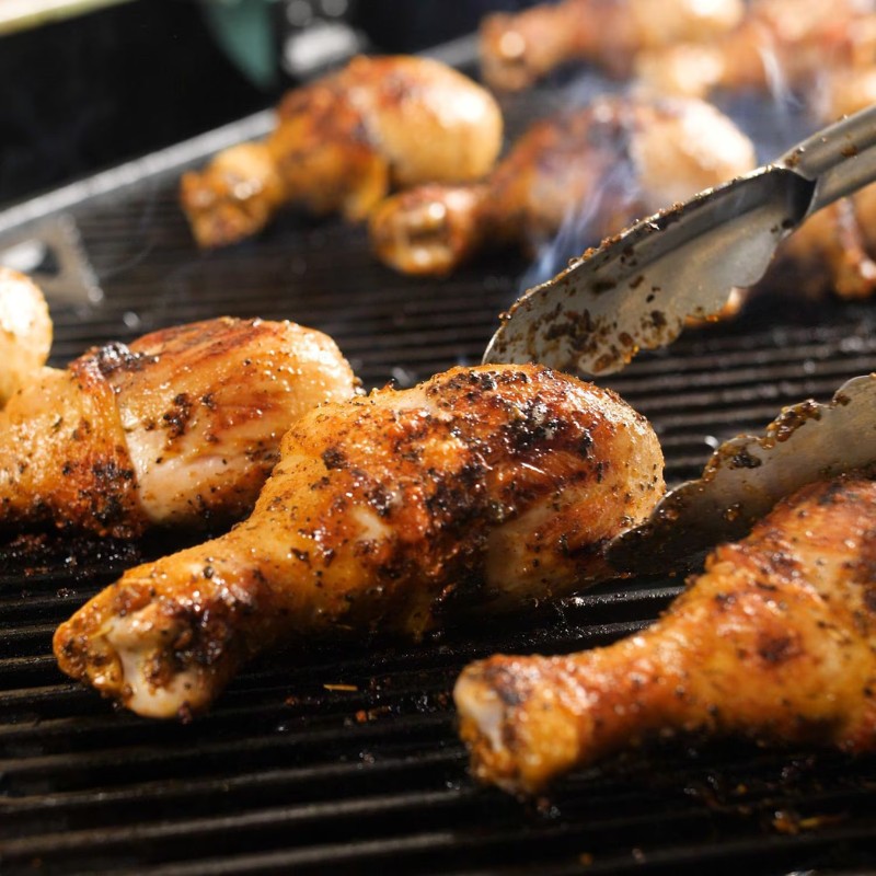 Grilled chicken drumsticks with smoky seasoning on a barbecue grill, showcasing a close-up of the cooking process.