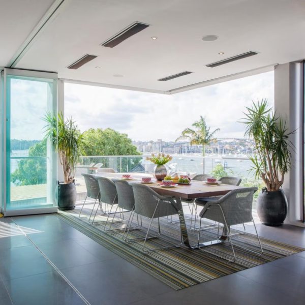 Modern dining area with large table, stylish chairs, and a view of the waterfront, featuring plants and natural light.