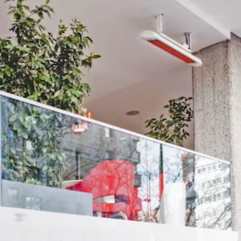 Modern outdoor seating area with glass railing, greenery, and a red chair, featuring overhead heating for comfort.