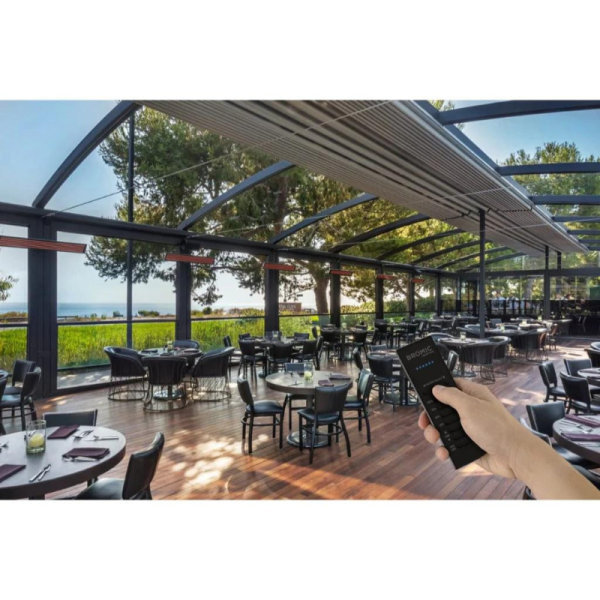 Modern restaurant interior with glass walls, featuring elegant tables and chairs, overlooking a scenic view. A hand holds a remote control for outdoor heating.
