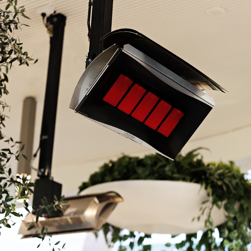 Hanging infrared heater with red heating elements, surrounded by greenery in a modern indoor setting.
