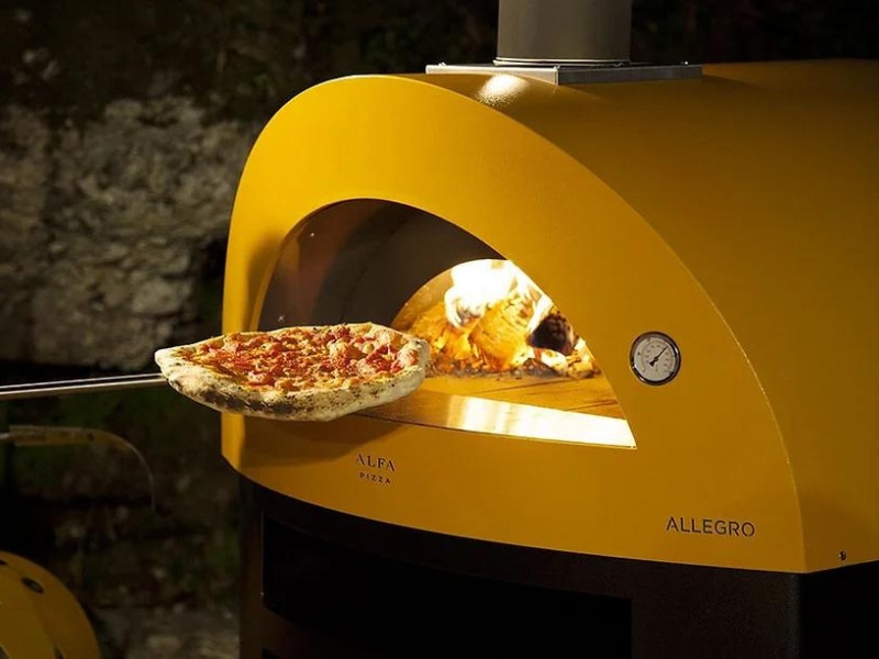 Pizza being pulled from a yellow wood-fired oven, showcasing the cooking process with flames visible inside.