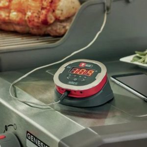 Digital meat thermometer displaying temperature on a grill with roasted meat in the background, showcasing precision cooking tools for grilling enthusiasts.
