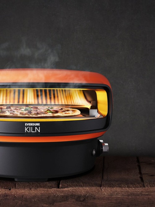 Everdure Kiln outdoor pizza oven with a freshly baked pizza inside, emitting steam, set against a dark background.