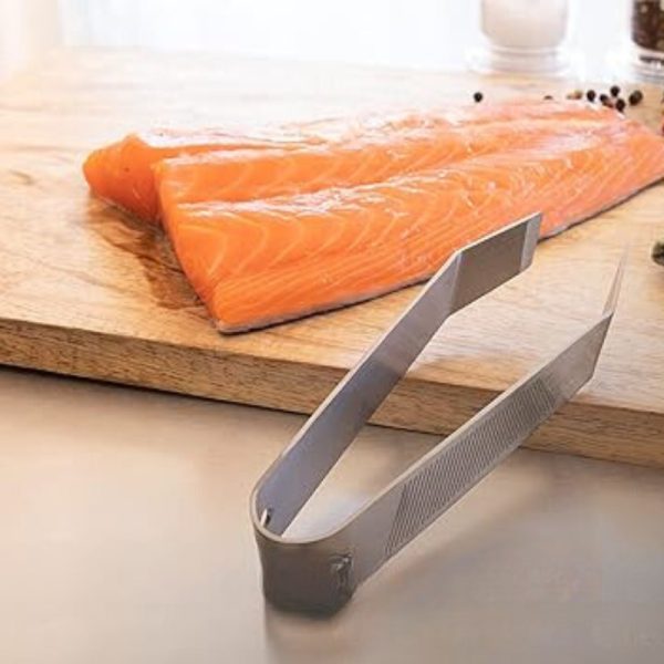 Stainless steel kitchen tongs next to fresh salmon fillets on a wooden cutting board, ideal for cooking and serving seafood.