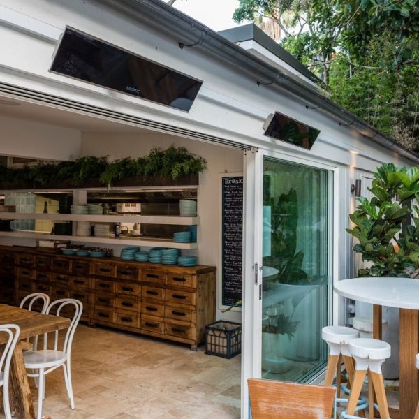 Bright and airy café interior with wooden furniture, open kitchen, and green plants, showcasing a modern design and inviting atmosphere.