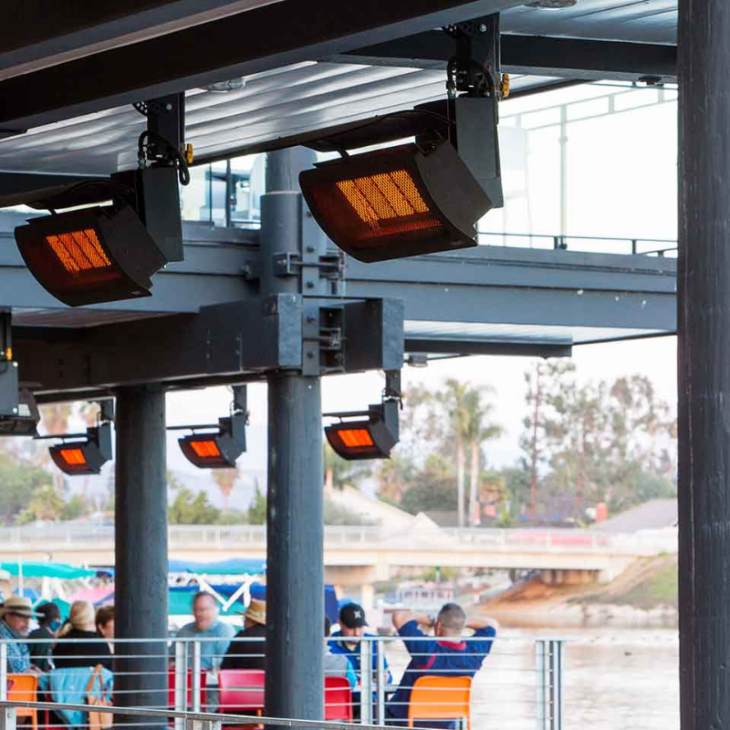 Outdoor heating lamps installed under a covered patio, providing warmth to guests seated near a waterfront.
