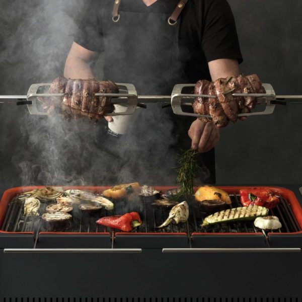 Grilling meat and vegetables on a barbecue, with smoke rising and a chef using a rotisserie for cooking.