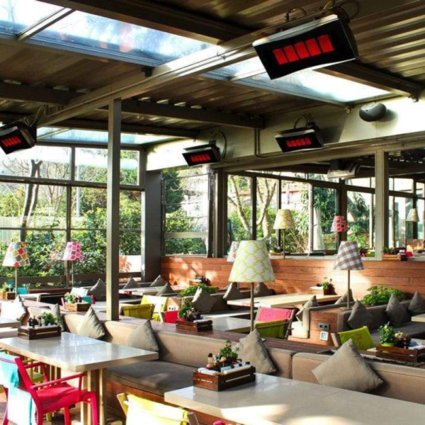 Cozy restaurant interior featuring glass walls, colorful seating, and decorative lamps, with heating panels on the ceiling for comfort.