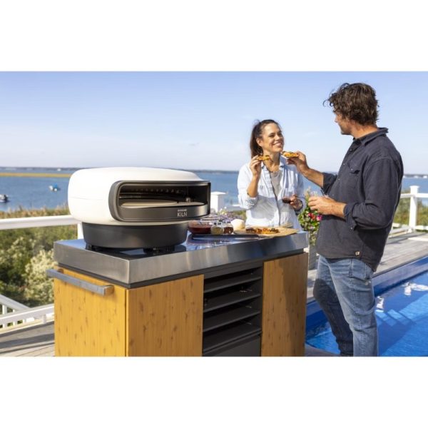 Couple enjoying pizza outdoors by a modern grill, with a scenic waterfront view. Ideal for outdoor cooking and entertaining.