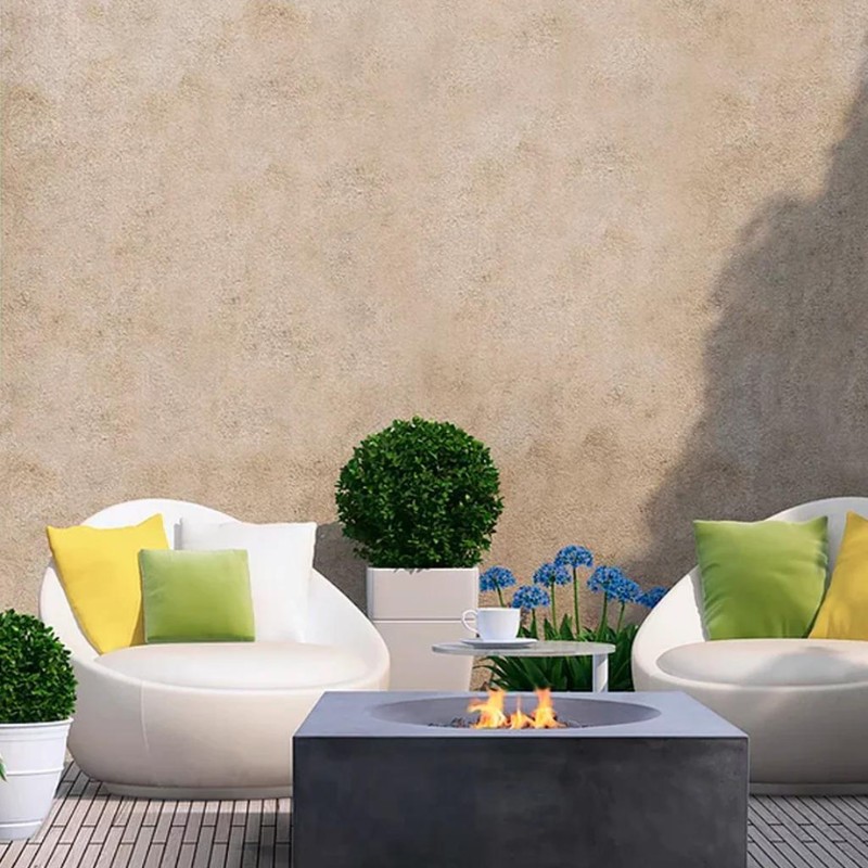 Modern outdoor lounge area with two white chairs, colorful cushions, a stone fire pit, and potted plants against a textured wall.
