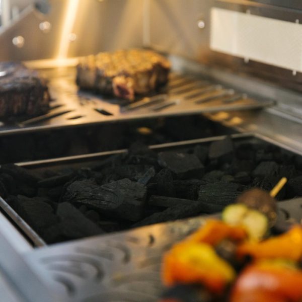 Grilling steaks and vegetable skewers over charcoal in a modern barbecue grill.