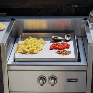 Coyote griddle cooking breakfast with scrambled eggs, cherry tomatoes, and avocado halves on a stainless steel surface.