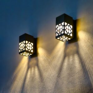 Two modern wall sconces with intricate geometric designs casting warm light and shadows on a textured wall.