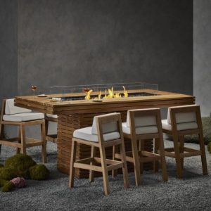 Modern outdoor fire table with wooden seating and glass wind guard, surrounded by decorative stones and greenery.