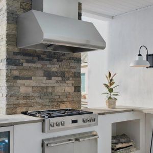 Modern kitchen featuring a stainless steel range hood above a gas stove, set against a stylish stone backsplash, with a potted plant and pendant light for added decor.