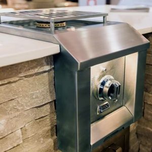 Stainless steel outdoor gas burner integrated into a stone countertop, featuring a control knob and grill grate.