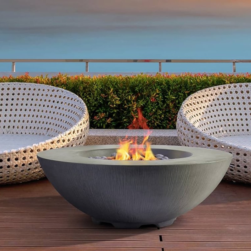 Modern outdoor fire pit surrounded by stylish woven chairs, with a serene background of greenery and a tranquil sky.