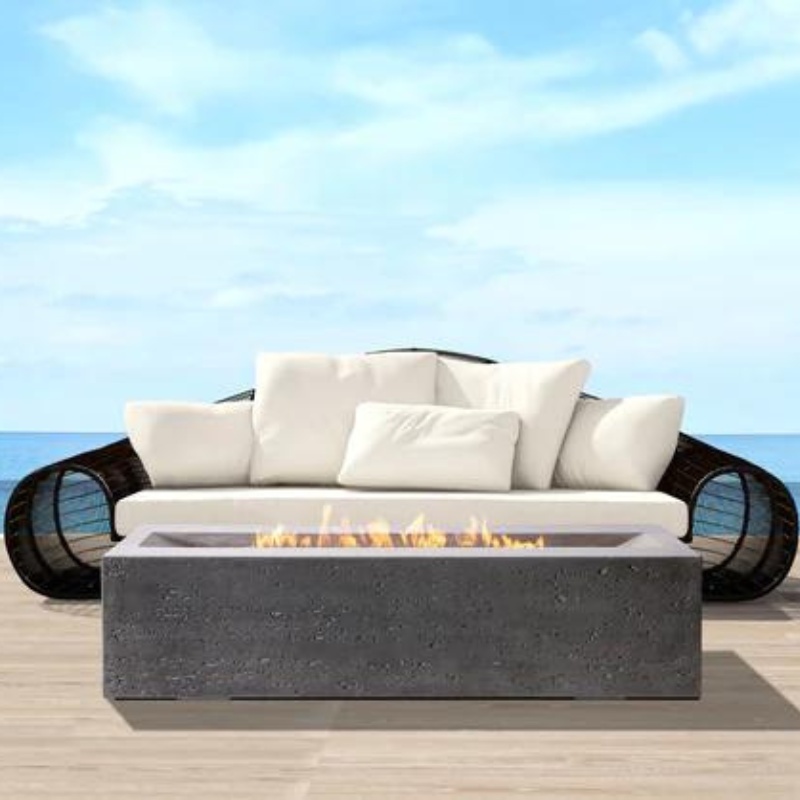 Modern outdoor seating area with a white sofa and a gray fire pit, overlooking a serene ocean view under a clear blue sky.