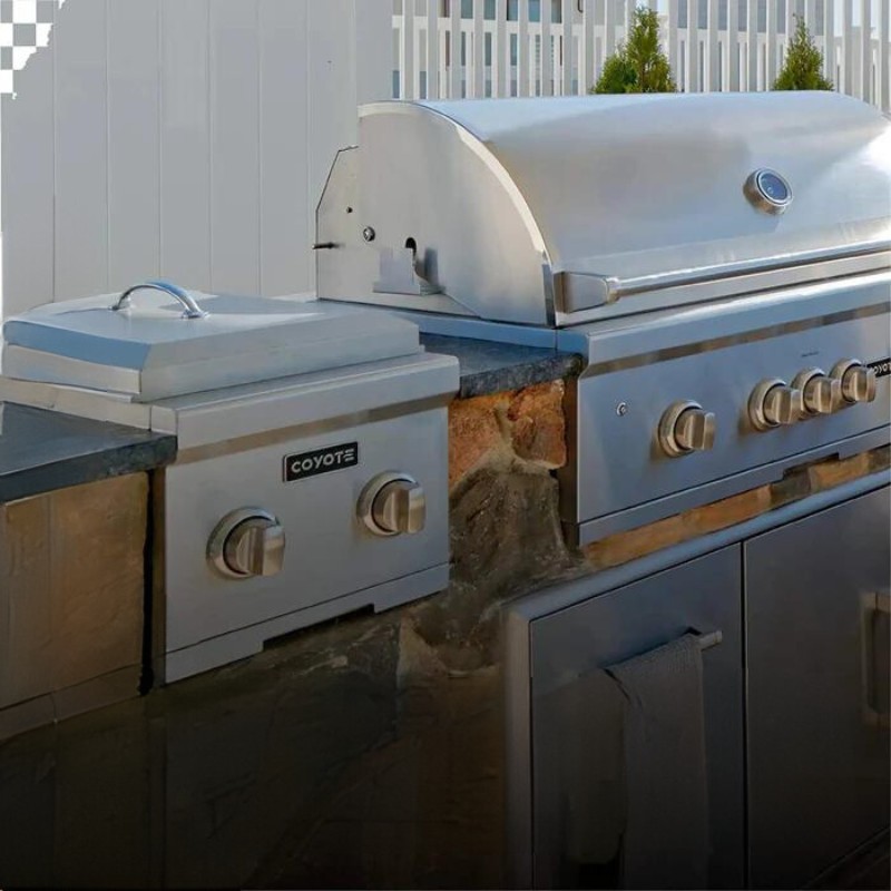 Stainless steel outdoor kitchen grill and side burner by Coyote, featuring a sleek design and stone countertop, ideal for backyard barbecues.
