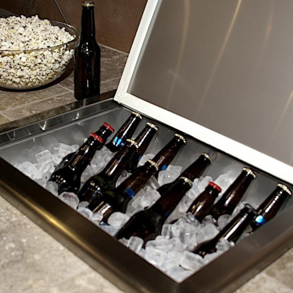 Bottles of beer chilling on ice in a stainless steel cooler, with a bowl of popcorn in the background.